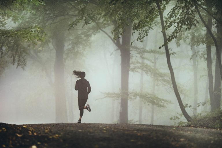 Une jeune femme court dans des sous bois à travers une brume
