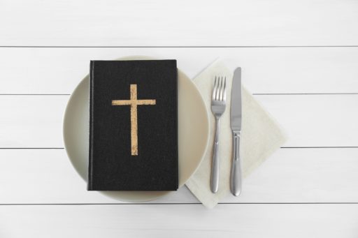 Une bible est posée sur une assiette, avec des couverts à côté