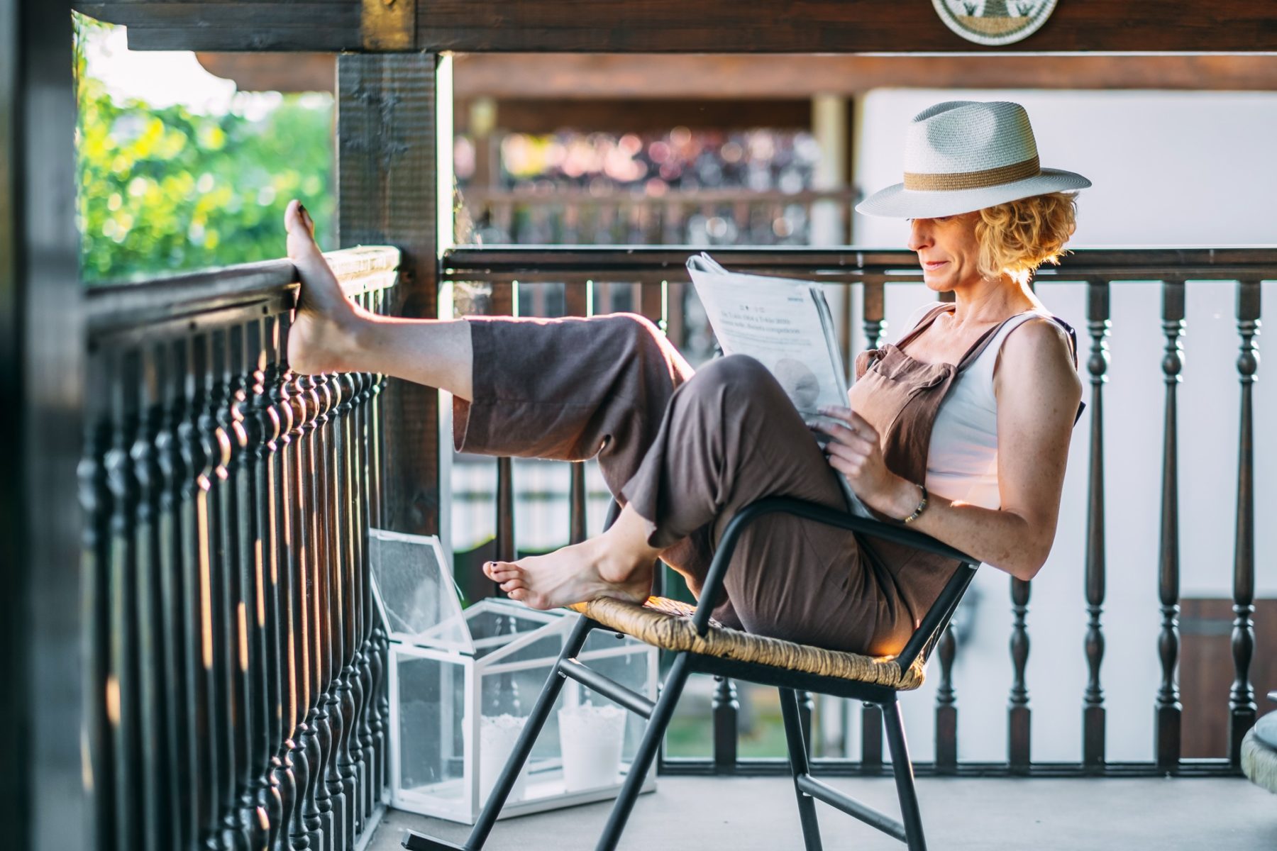 Une dame lit, assise et très détendue sur son balcon. Elle porte un chapeau